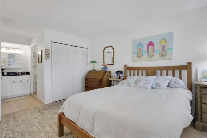 Bedroom featuring light wood-finish flooring, a white bi-fold closet, and a vanity area with white cabinetry and dark countertops
