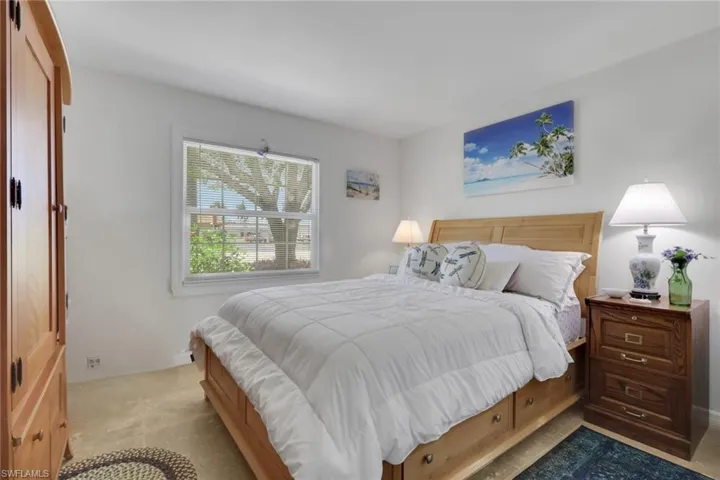 Carpeted bedroom with a natural wood-finish bed frame featuring integrated drawers, white walls, and a double-hung window