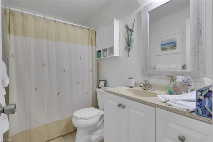 Bathroom featuring a single vanity with a stone-finish countertop, white cabinetry, and a framed mirror