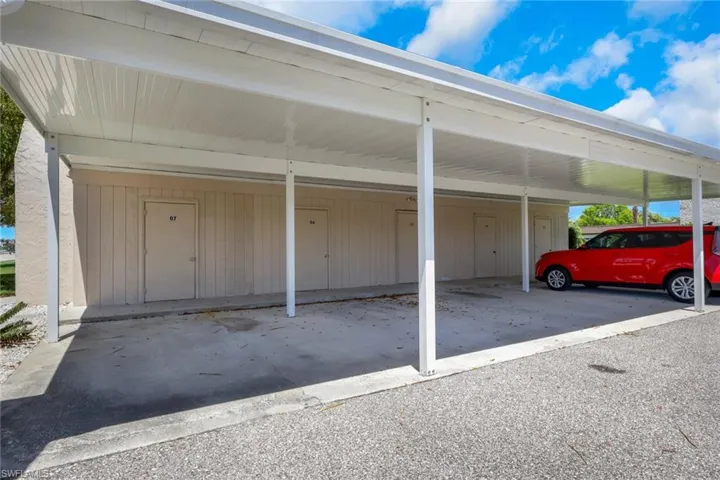 Covered parking area featuring a white metal carport structure, concrete pad, and individual storage units with numbered doors