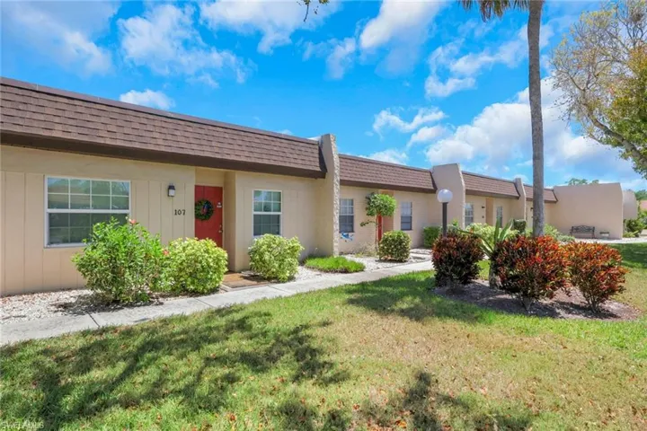 Unit 107 exterior featuring a red entry door, white-framed windows, and a brown shingle roof