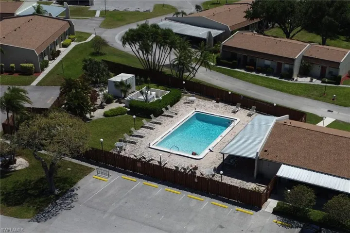 Rectangular outdoor swimming pool surrounded by a sand-colored deck, multiple lounge chairs, and a metal-roofed covered patio
