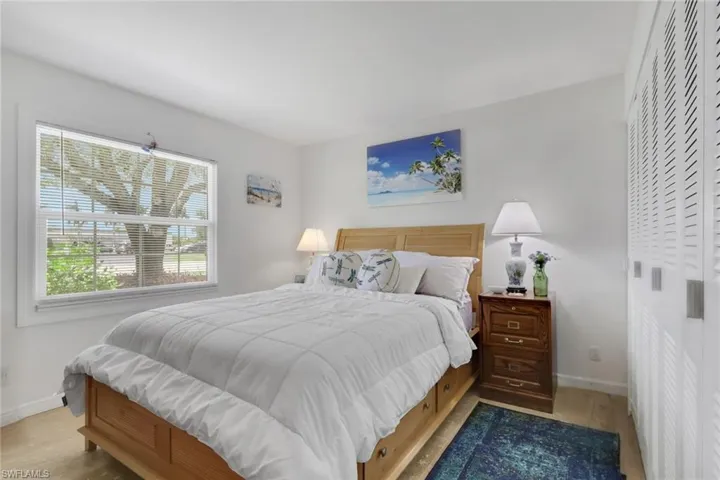 Bedroom featuring a large window, light-toned wood-finish flooring, white walls, and louvered bifold closet doors with silver-tone pulls