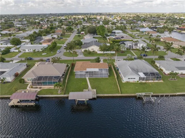 Aerial view of the canal, dock, covered boat lift, and fenced backyard.