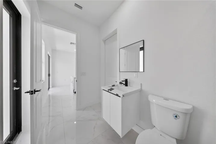 Bathroom featuring a white vanity with integrated sink, black single-handle faucet, rectangular mirror, and a white toilet