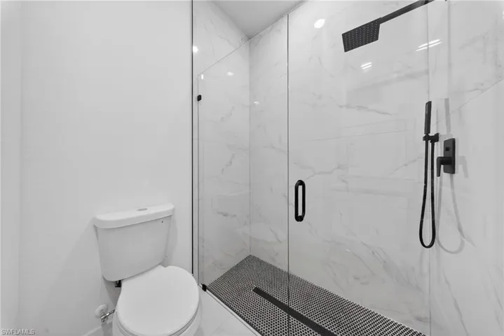 Enclosed shower with clear glass panels, marble-look tile walls, and a black penny tile floor