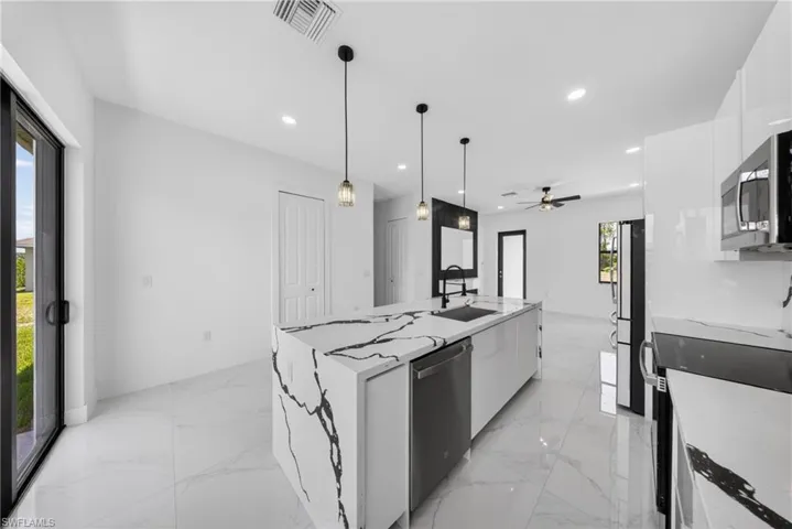 Modern kitchen featuring a waterfall island with a dark veined countertop, stainless steel appliances, white cabinetry, and recessed lighting