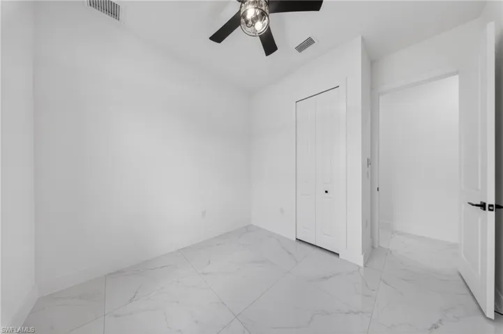 Room featuring white walls, large format tile flooring, a ceiling fan with light fixture, and a bi-fold closet door