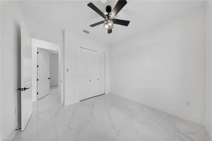 Room featuring marble-look floor tile, a modern ceiling fan with integrated lighting, white paneled doors with black hardware, and bi-fold closet doors