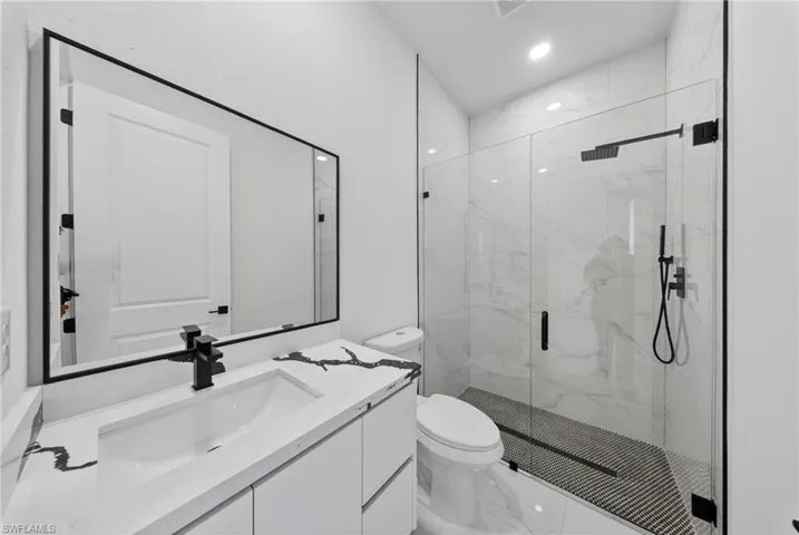Contemporary bathroom featuring a frameless glass shower enclosure, white and gray veined wall tile, and a black mosaic tile shower floor