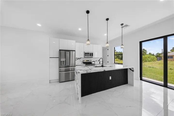 Modern kitchen featuring a waterfall island with a black slatted base, white countertops, and three pendant lights