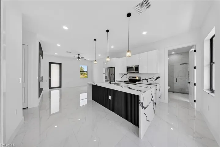 Kitchen featuring a large waterfall island with a black slatted base, white high-gloss cabinetry, integrated stainless steel appliances, pendant lighting, and polished tile flooring
