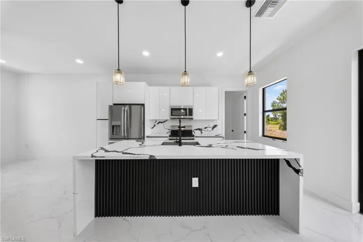 Modern kitchen featuring a waterfall island with a black slatted base, white countertops with prominent black veining, and three pendant lights