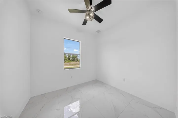 Bright interior space featuring white walls, large format tile flooring, and a modern ceiling fan with integrated lighting