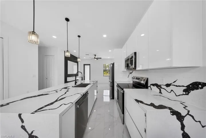 Modern kitchen featuring an expansive island with a waterfall-edge countertop, black and white veined surfaces, sleek white cabinetry, and stainless steel appliances