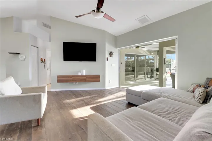 Living area featuring visible vents, baseboards, ceiling fan, vaulted ceiling, and hardwood / wood-style flooring