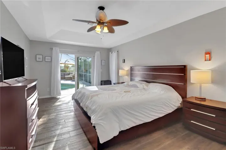 Bedroom with access to exterior, ceiling fan, baseboards, a tray ceiling, and hardwood / wood-style floors