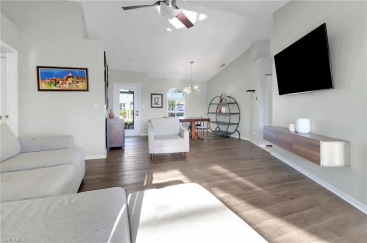 Living area featuring wood finished floors, ceiling fan with notable chandelier, baseboards, and high vaulted ceiling