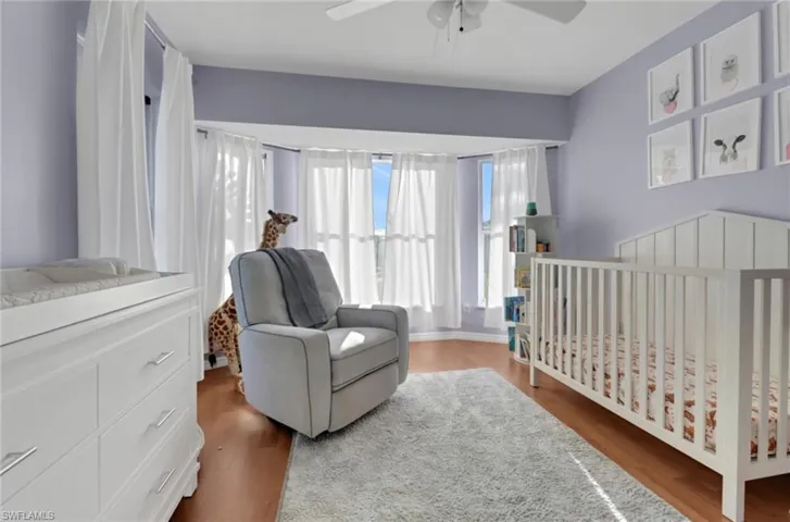 Bedroom with a ceiling fan, a nursery area, and wood finished floors