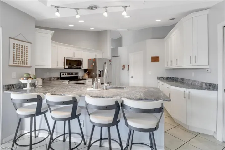 Kitchen with light tile patterned floors, a peninsula, a sink, appliances with stainless steel finishes, and white cabinetry