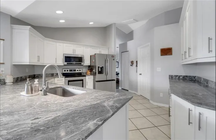 Kitchen with vaulted ceiling, light tile patterned floors, appliances with stainless steel finishes, white cabinets, and a sink