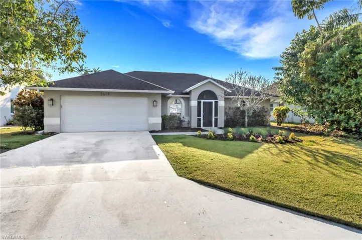 Ranch-style home featuring a front lawn, an attached garage, driveway, and stucco siding