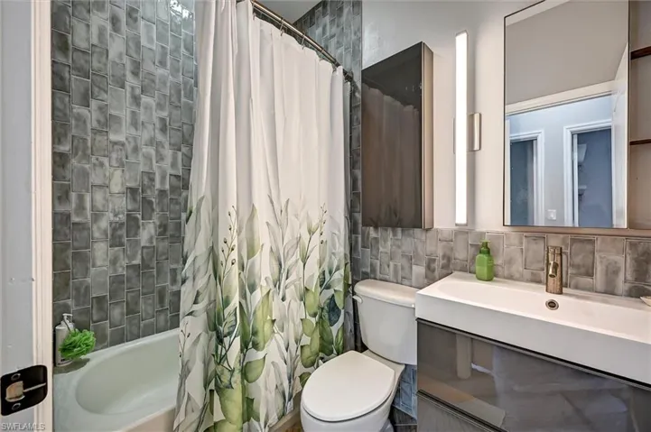 Full bath with vanity, shower / bath combination with curtain, tile walls, and tasteful backsplash