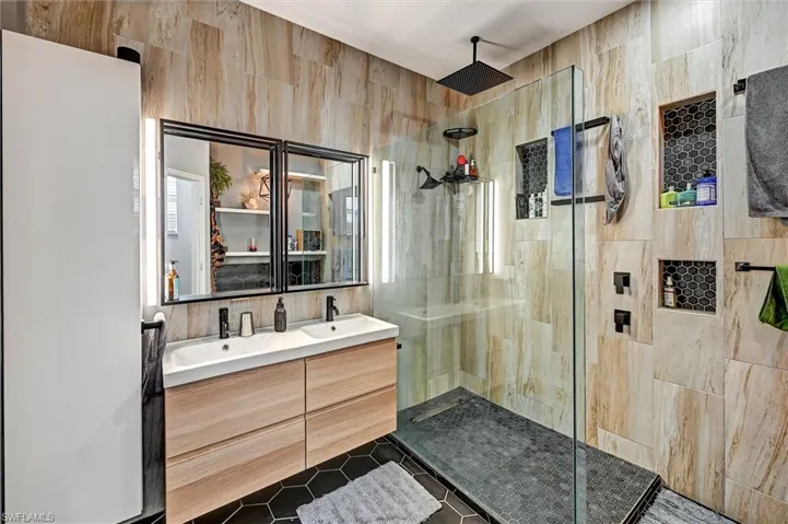 Full bath featuring double vanity, a walk in shower, and dark tile patterned floors