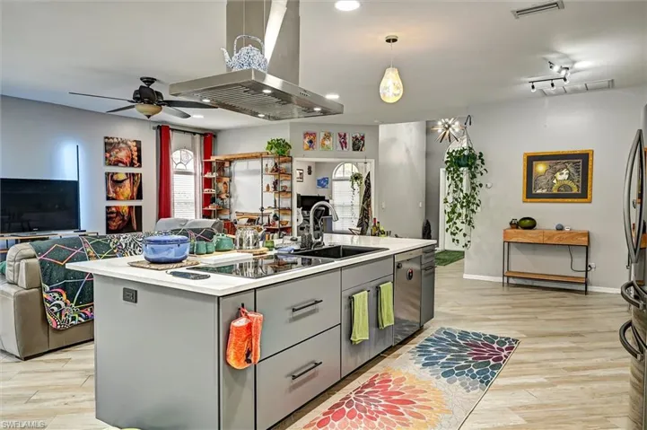 Kitchen featuring open floor plan, island range hood, an island with sink, light wood-type flooring, and ceiling fan