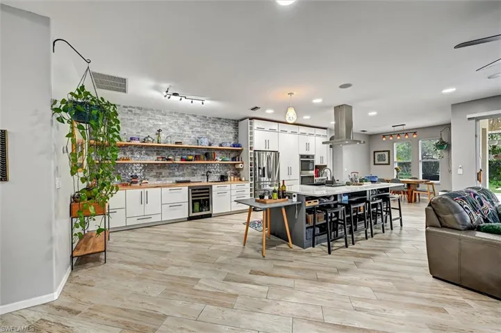 Two tone kitchen featuring a breakfast bar, an island with sink, dual tone cabinetry, light wood-type flooring, and island exhaust hood