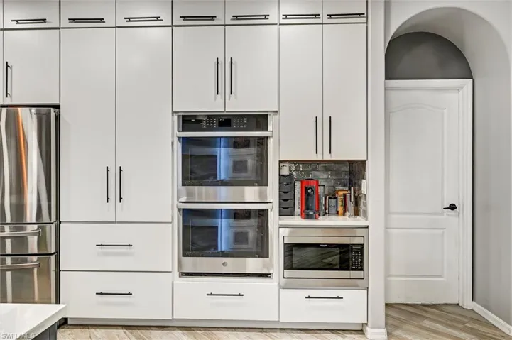 Kitchen featuring stainless steel appliances, light wood finished floors, white cabinetry, and backsplash