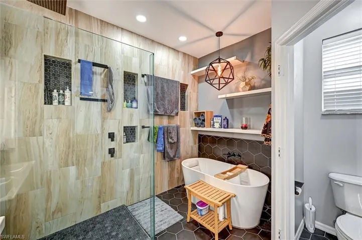 Full bathroom featuring walk in shower, dark tile patterned flooring, a freestanding tub, recessed lighting, and tile walls