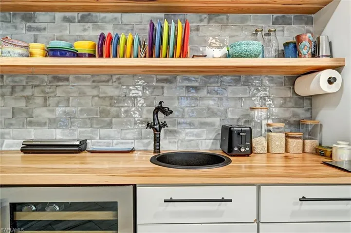 Kitchen view of beverage cooler, white cabinets, wood counters, and backsplash