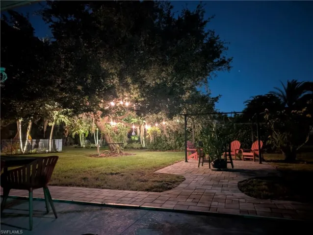 Expansive backyard featuring a paver patio, string lighting, mature trees, and landscape lighting