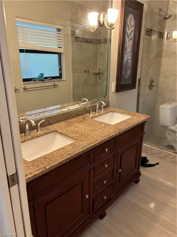 Full bath with double vanity, a shower stall, and light wood-style flooring