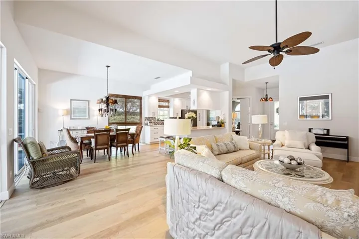 Living area with light wood-type flooring, a ceiling fan, plenty of natural light, a chandelier, and a high ceiling