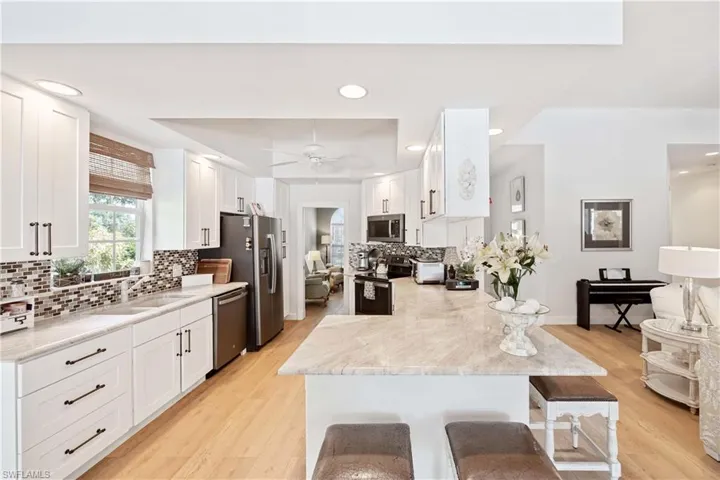 Kitchen with marble counters  and stainless steel appliances, a sink, a breakfast bar area, white cabinetry, and recessed lighting