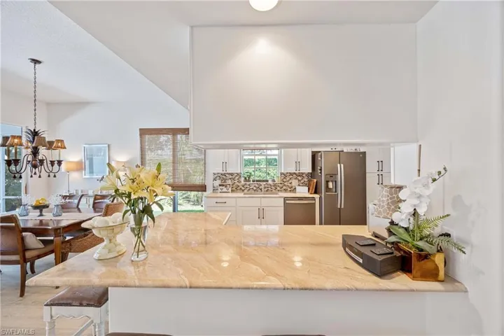 Kitchen with stainless steel appliances, white cabinetry, a sink, tasteful backsplash, and light stone countertops