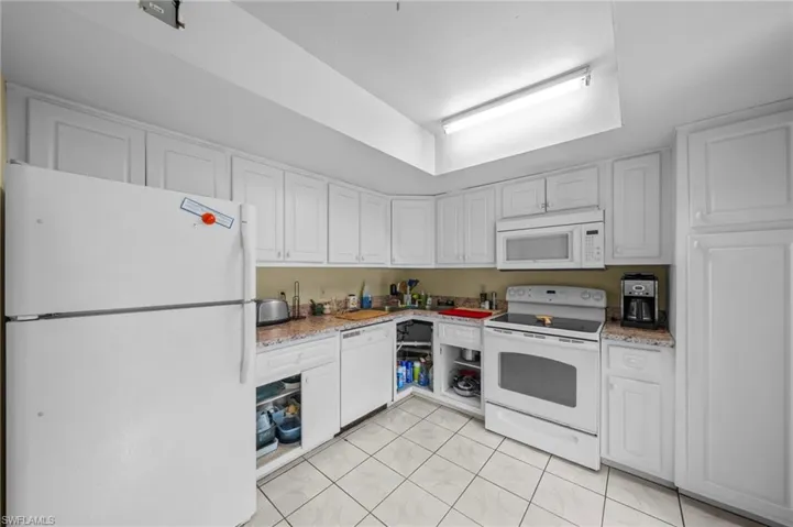 Kitchen with white appliances, white cabinetry, light tile patterned floors, and light stone counters