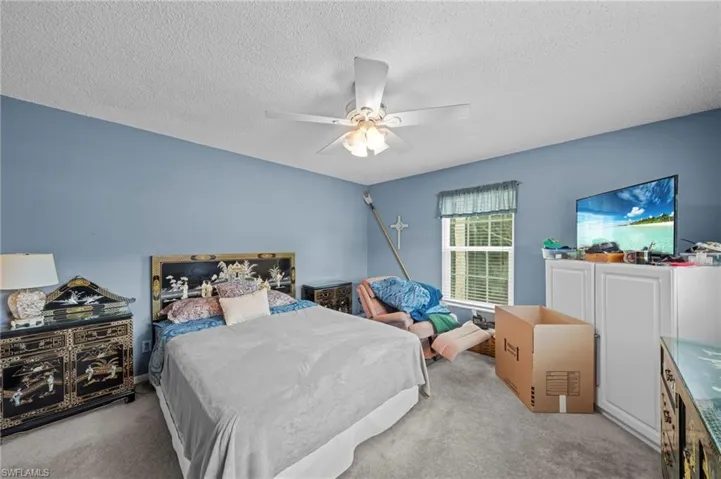 Bedroom with light colored carpet, ceiling fan, and a textured ceiling