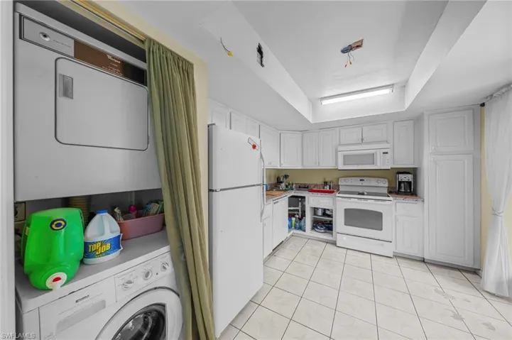Kitchen featuring light countertops, white appliances, a tray ceiling, stacked washer / dryer, and light tile patterned floors