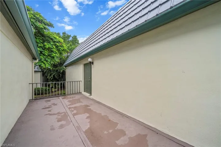 View of side of property with stucco siding, a patio, and mansard roof