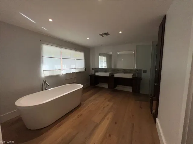 Full bath featuring double vanity, a soaking tub, light wood finished floors, and recessed lighting
