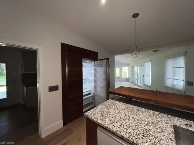Kitchen with lofted ceiling, light stone counters, dark wood-style floors, and pendant lighting