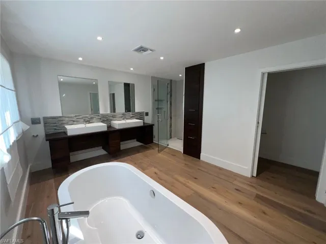 Bathroom featuring double vanity, a stall shower, a tub, tasteful backsplash, and wood finished floors