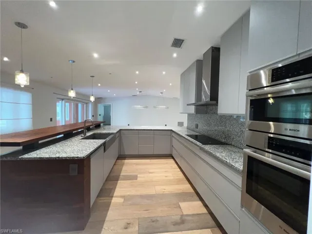 Kitchen featuring gray cabinets, light stone counters, modern cabinets, and stainless steel double oven