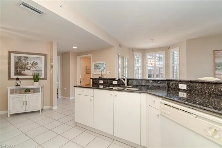 Kitchen with decorative light fixtures, dishwasher, sink, white cabinets, and dark stone counters