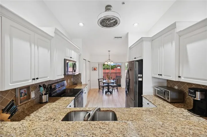 Kitchen with light wood-type flooring, tasteful backsplash, stainless steel appliances, sink, and white cabinetry