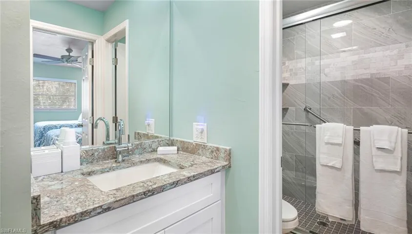 Bathroom with toilet, a stall shower, ceiling fan, and vanity