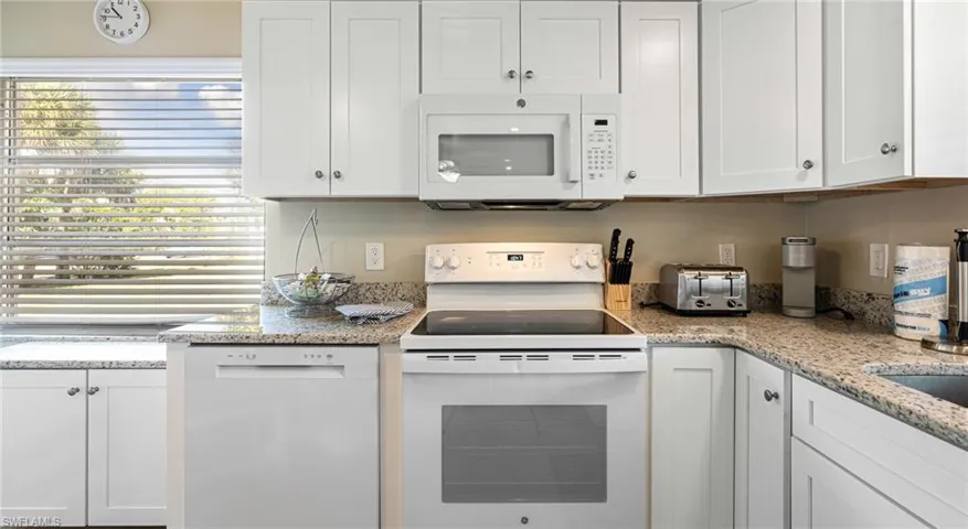Kitchen featuring a toaster, white appliances, light stone counters, and white cabinets